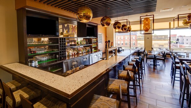 A bar area with a long counter, multiple seating options, and a large window offering a view of the city. - Delta Hotels by Marriott Saint John (Saint John)