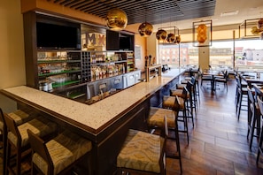 A bar area with a long counter, multiple seating options, and a large window offering a view of the city. - Delta Hotels by Marriott Saint John (Saint John)