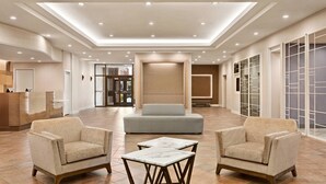 A spacious lobby with a reception desk, two armchairs, a sofa, and a marble coffee table. - Delta Hotels by Marriott Saint John (Saint John)