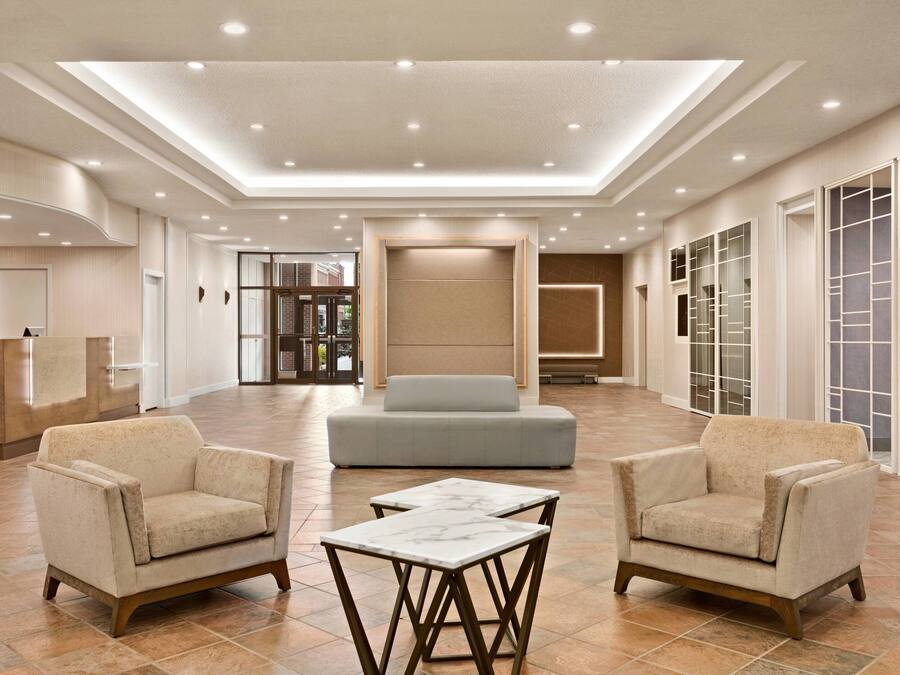 Um hall amplo com um balcão de recepção, duas poltronas, um sofá e uma mesa de centro de mármore.