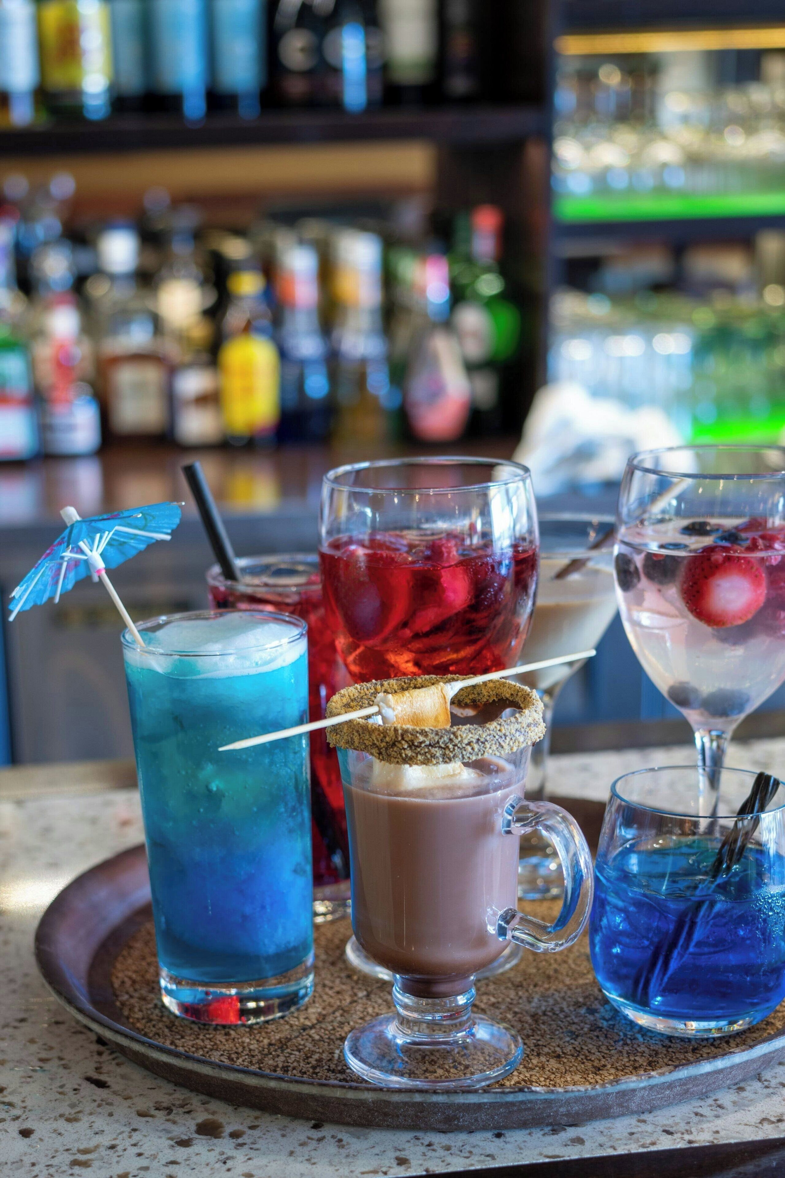 A tray with three drinks: a blue cocktail, a red drink, and a clear beverage with a straw.