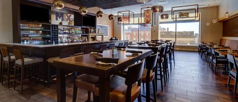 Un restaurante con zona de bar, mesas y sillas de madera.