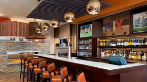 A bar area with a long counter, multiple stools, a television screen, and a variety of bottles and glasses. - Delta Hotels by Marriott Saint John (Saint John)