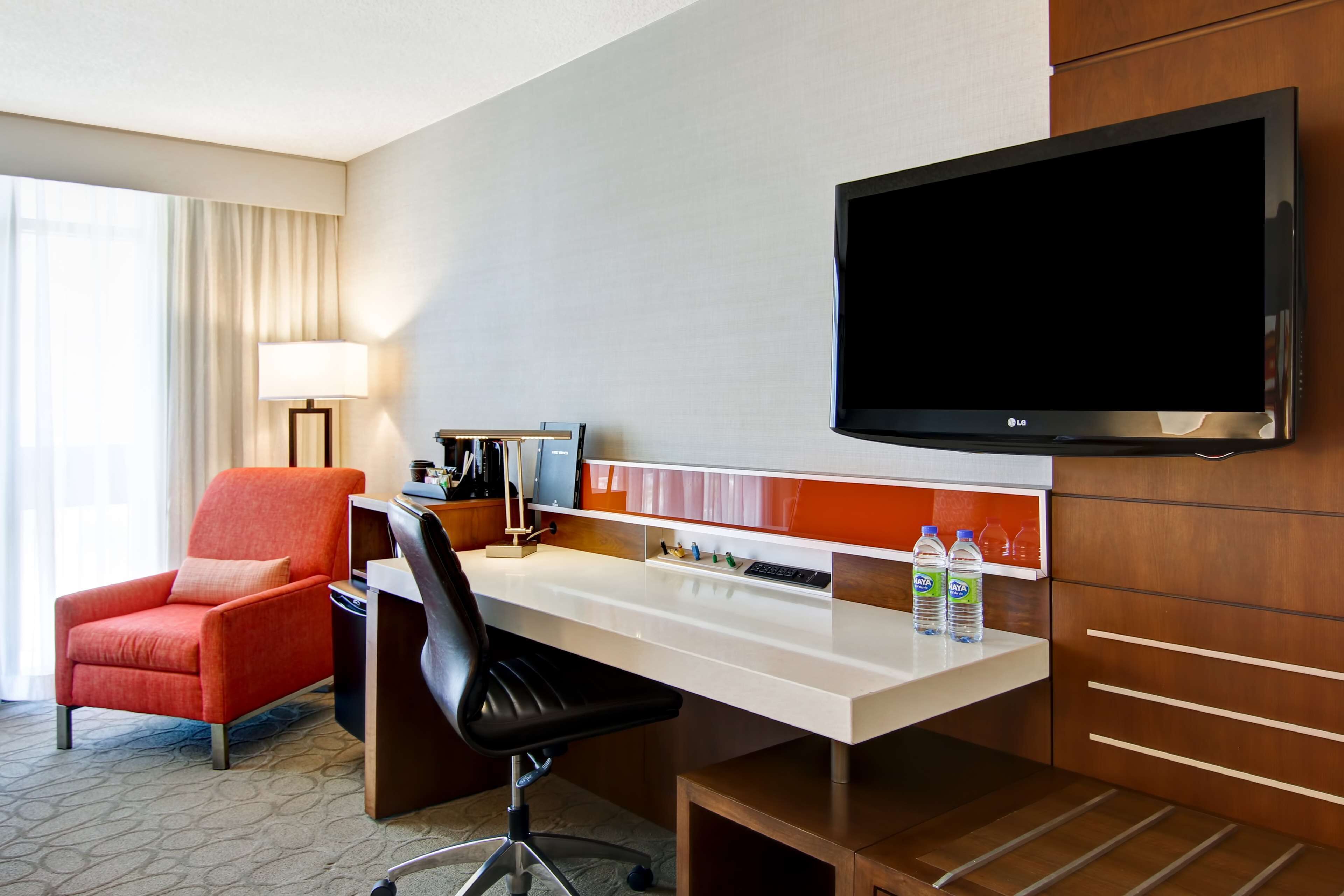 A hotel room with a desk, chair, TV, and a minibar.