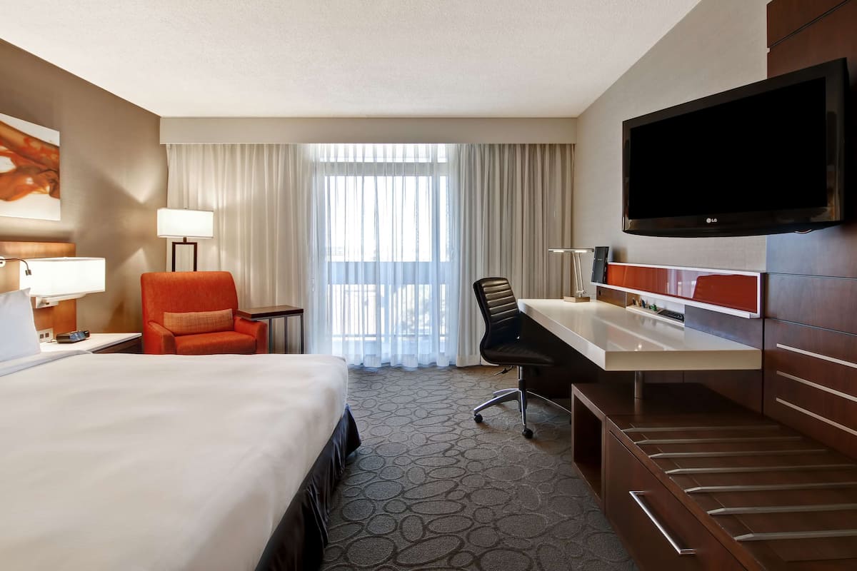 A hotel room with a bed, desk, chair, TV, and curtains.
