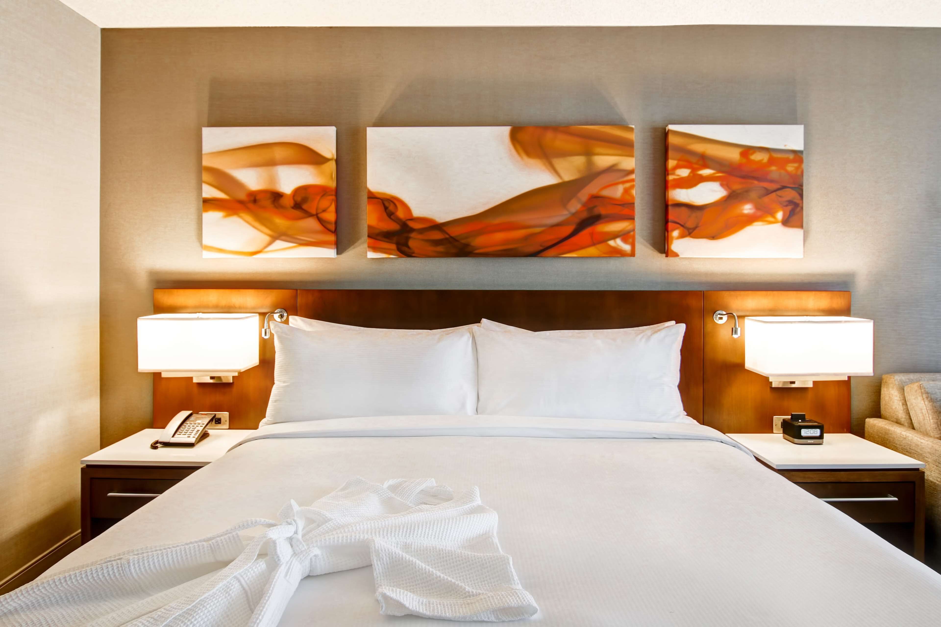 Una habitación de hotel con una cama grande, dos mesitas de noche con lámparas, un teléfono y una obra de arte colgada en la pared.