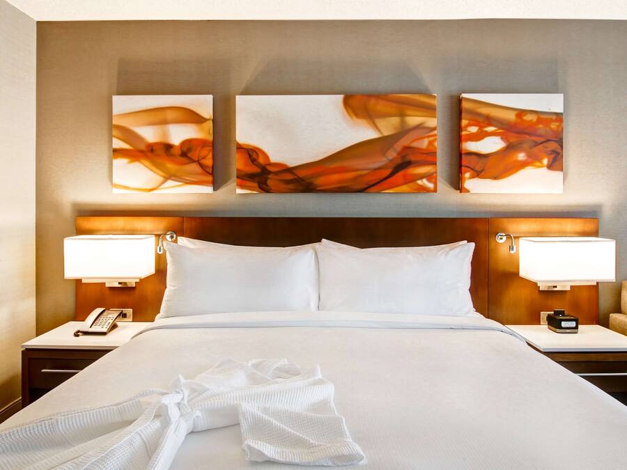 Una habitación de hotel con una cama grande, dos mesitas de noche con lámparas, un teléfono y una obra de arte colgada en la pared.