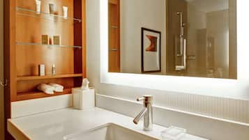 Un baño moderno con un espejo grande, un lavabo blanco y estantes de madera con artículos de aseo.
