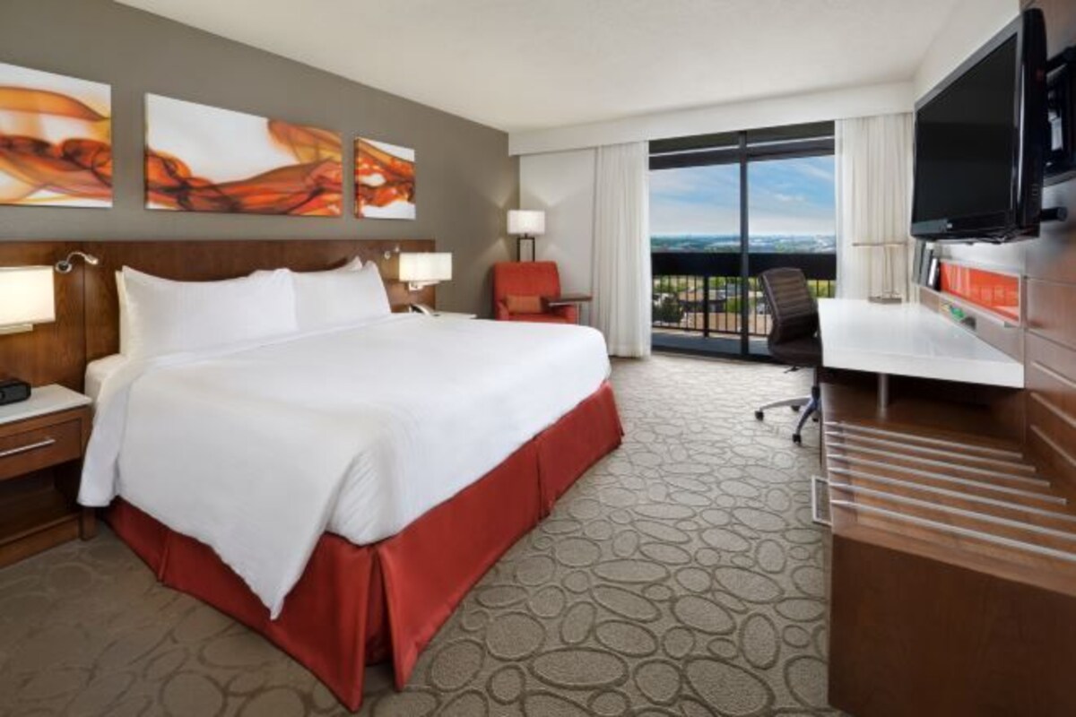 A hotel room with a large bed, a desk with a TV, and a view of the city.