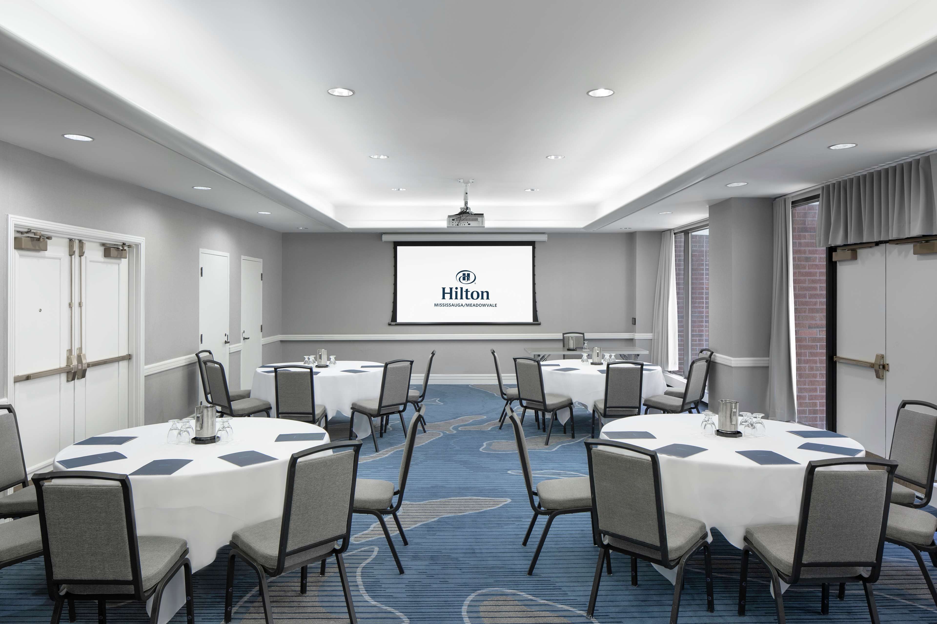 A conference room with round tables, chairs, a projector screen, and a carpeted floor.