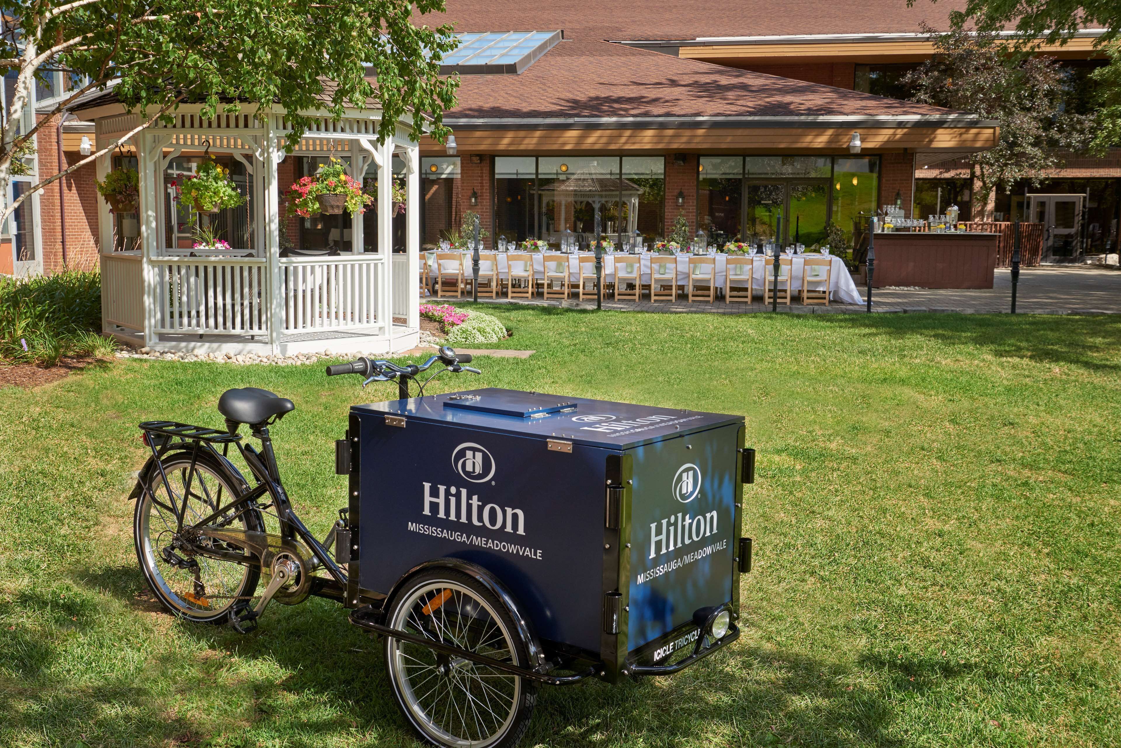 A bicycle with a delivery box parked on grass in front of a building with a covered outdoor seating area.