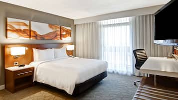 A hotel room with a large bed, a desk, a chair, and a TV.