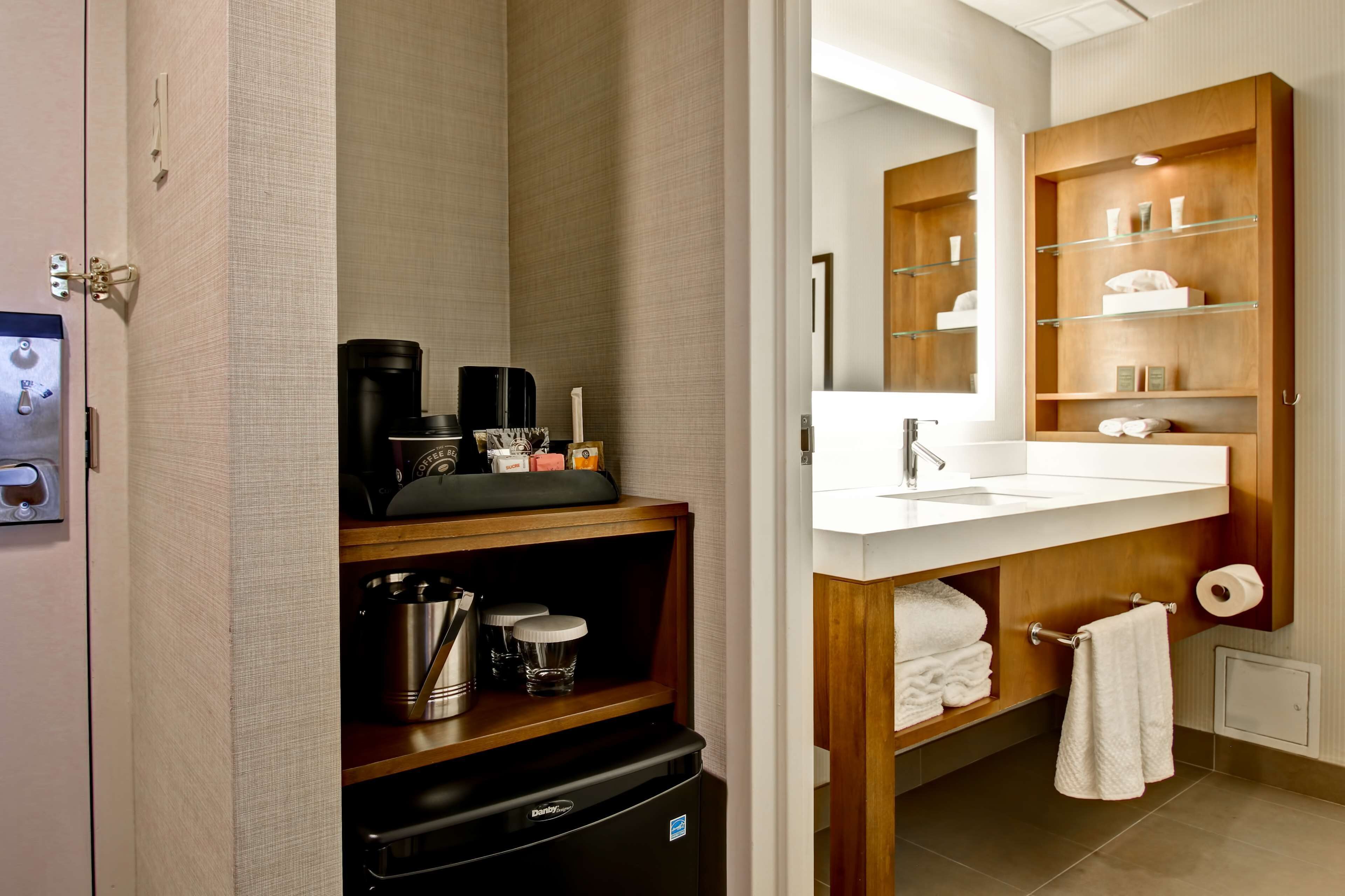 A modern bathroom with a wooden vanity, a built-in coffee maker, and a mirror above the sink.
