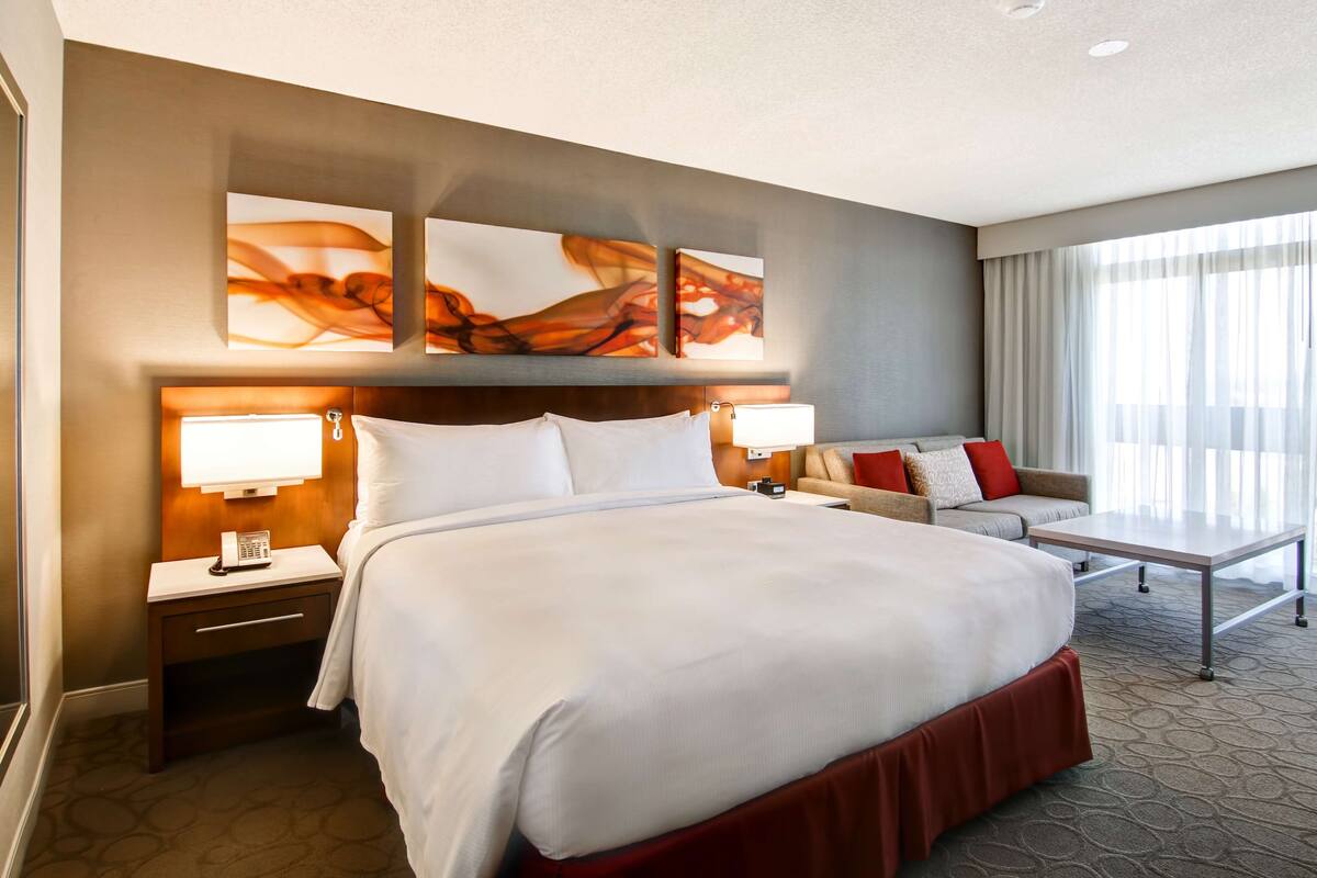 A hotel room with a large bed, bedside tables, a sofa, and abstract wall art.