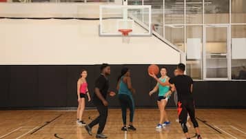 Un groupe de personnes joue au basketball dans un gymnase, sur un terrain avec un panier et un plancher en bois.