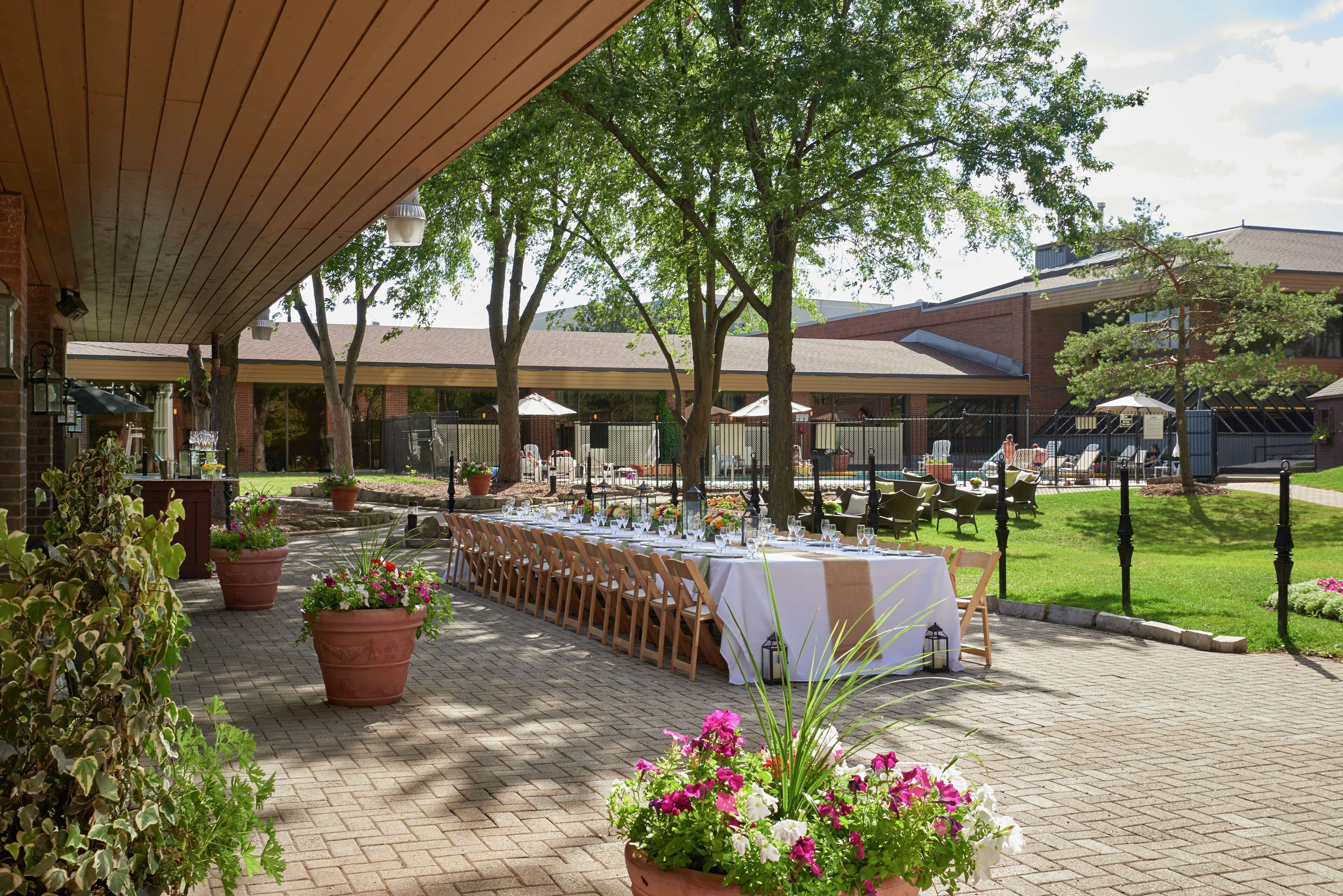 An outdoor dining area with tables set for a meal, surrounded by potted plants and trees.