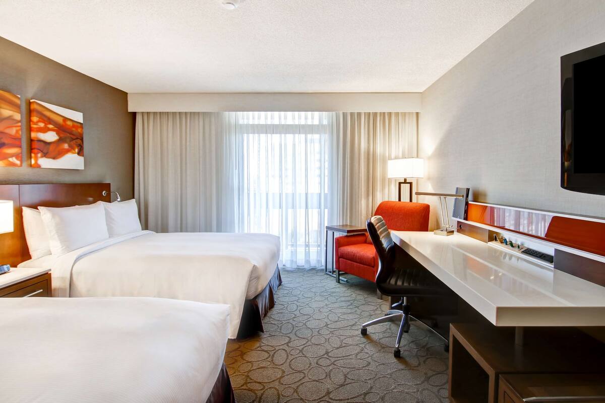 A hotel room with two beds, a desk, a chair, a TV, and a window with curtains.