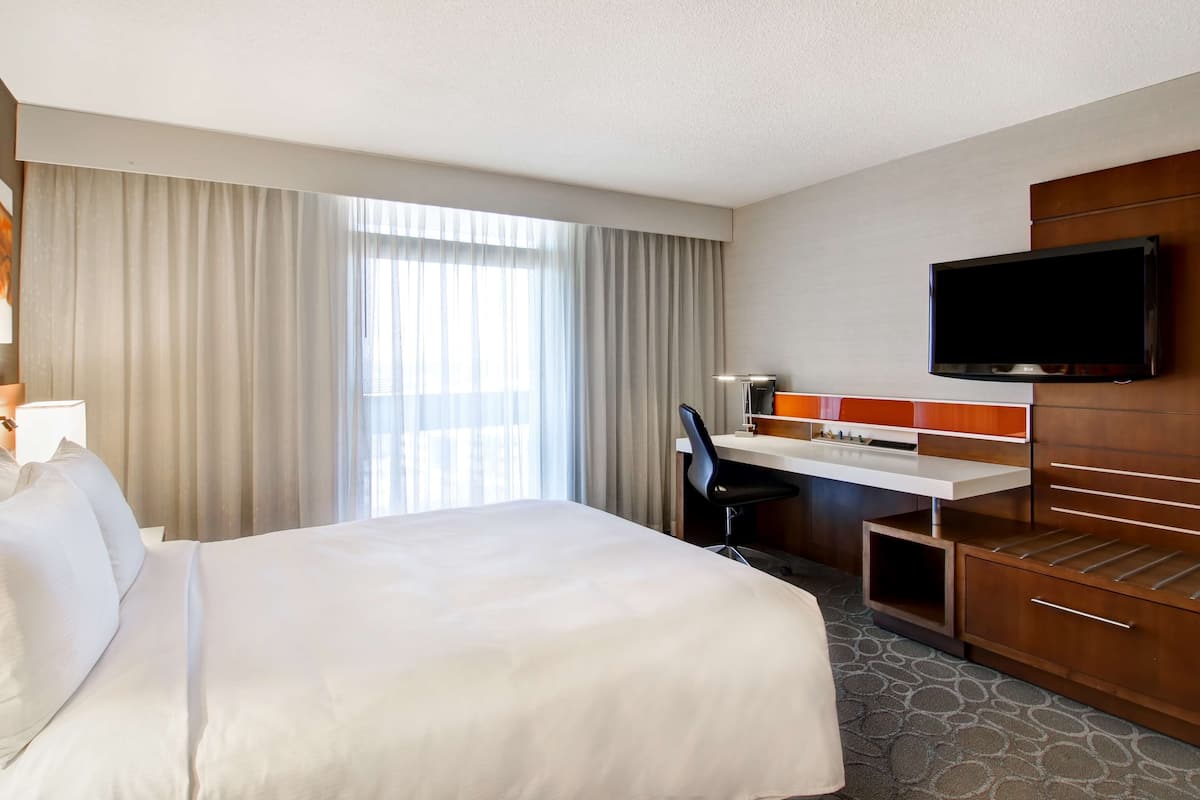 A hotel room with a large bed, a desk, a chair, a television, and a minibar.