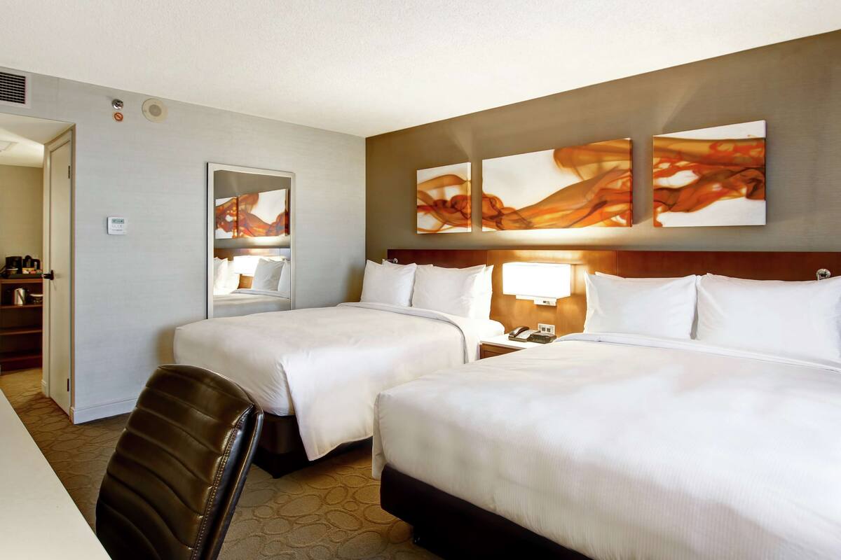 A hotel room with two beds, a desk, a chair, and artwork on the wall.