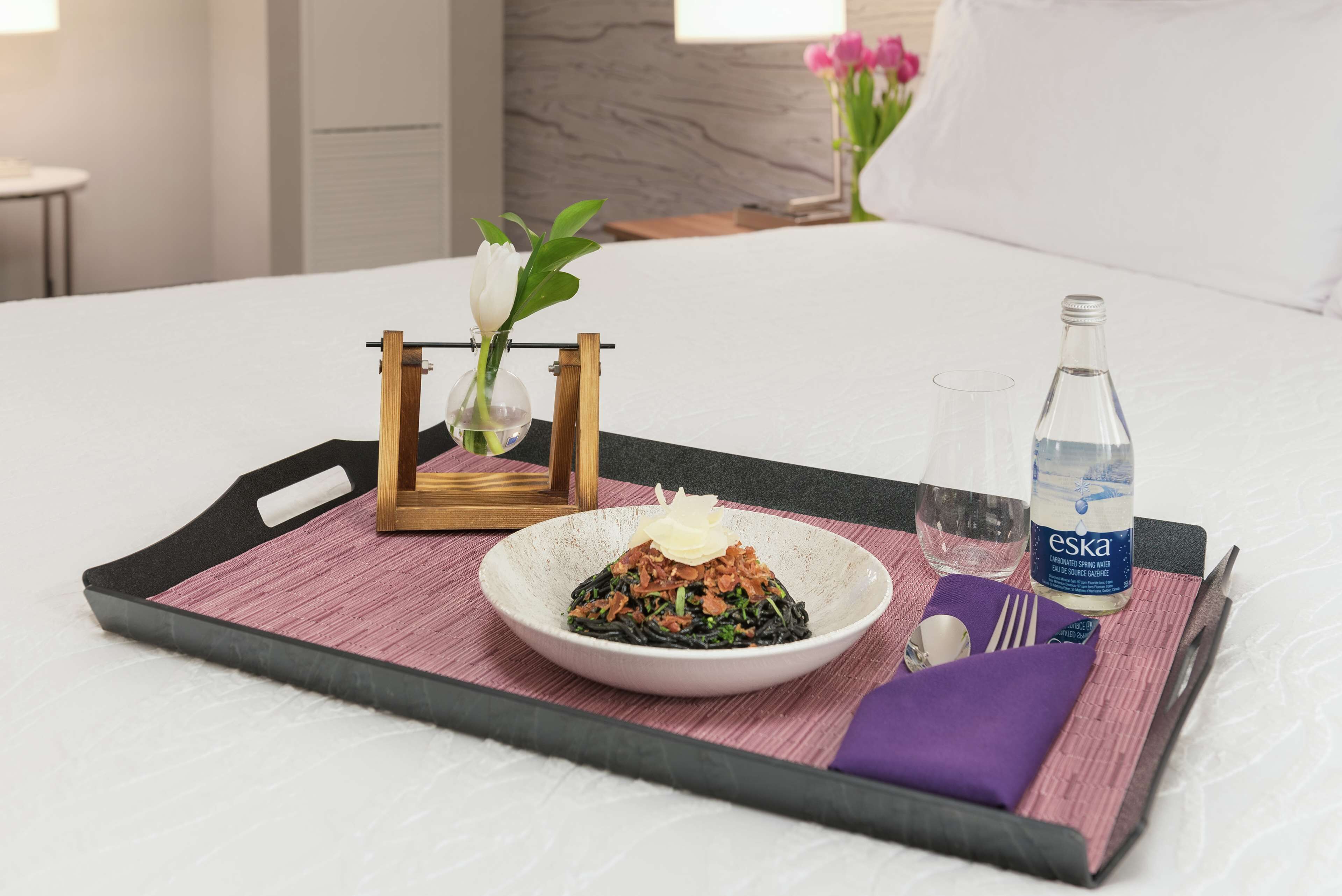 Ein ordentlich gedeckter Frühstückstisch mit einer Nudelschüssel, einem Glas Wasser und einer Wasserflasche auf einem Bett.