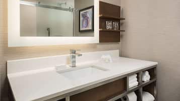 A modern bathroom with a large mirror, a white sink, and a wooden vanity with shelves holding towels and toiletries.