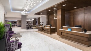 Un hall d’hôtel moderne avec un sol en marbre, un comptoir d’accueil et des sièges violets.