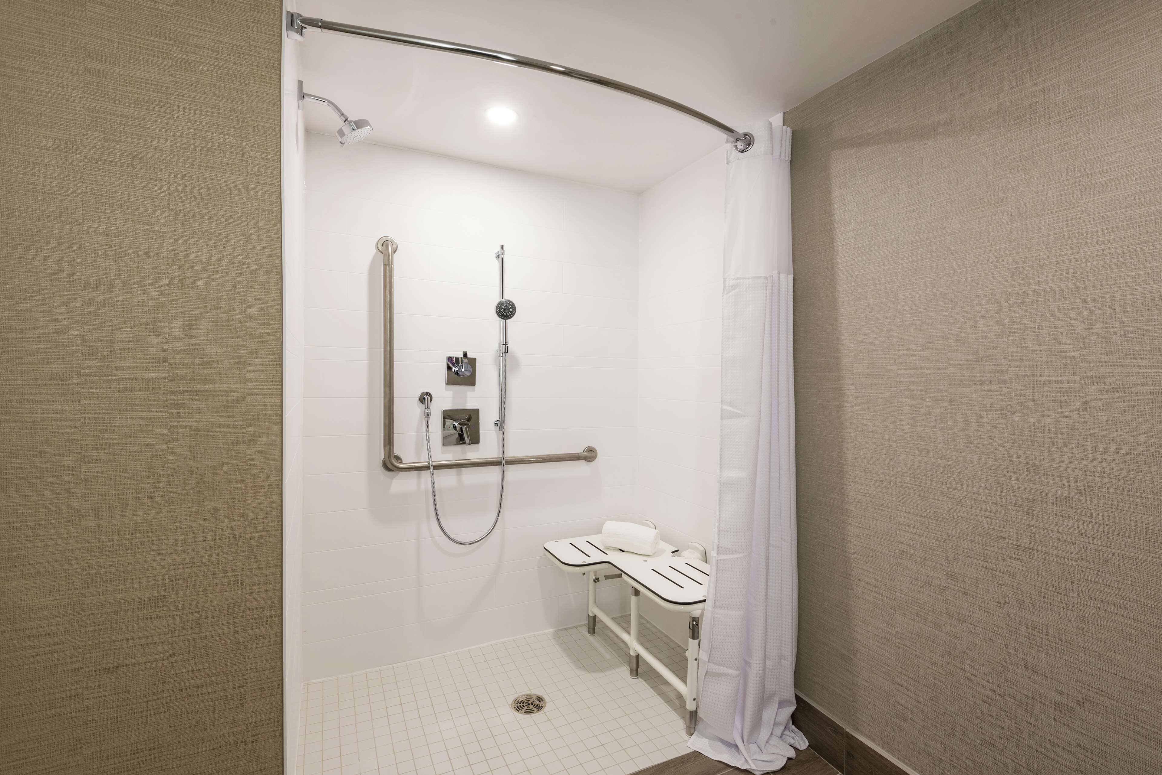 A modern bathroom with a walk-in shower, grab bars, and a white sink.