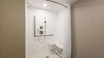 A modern bathroom with a walk-in shower, grab bars, and a white sink.