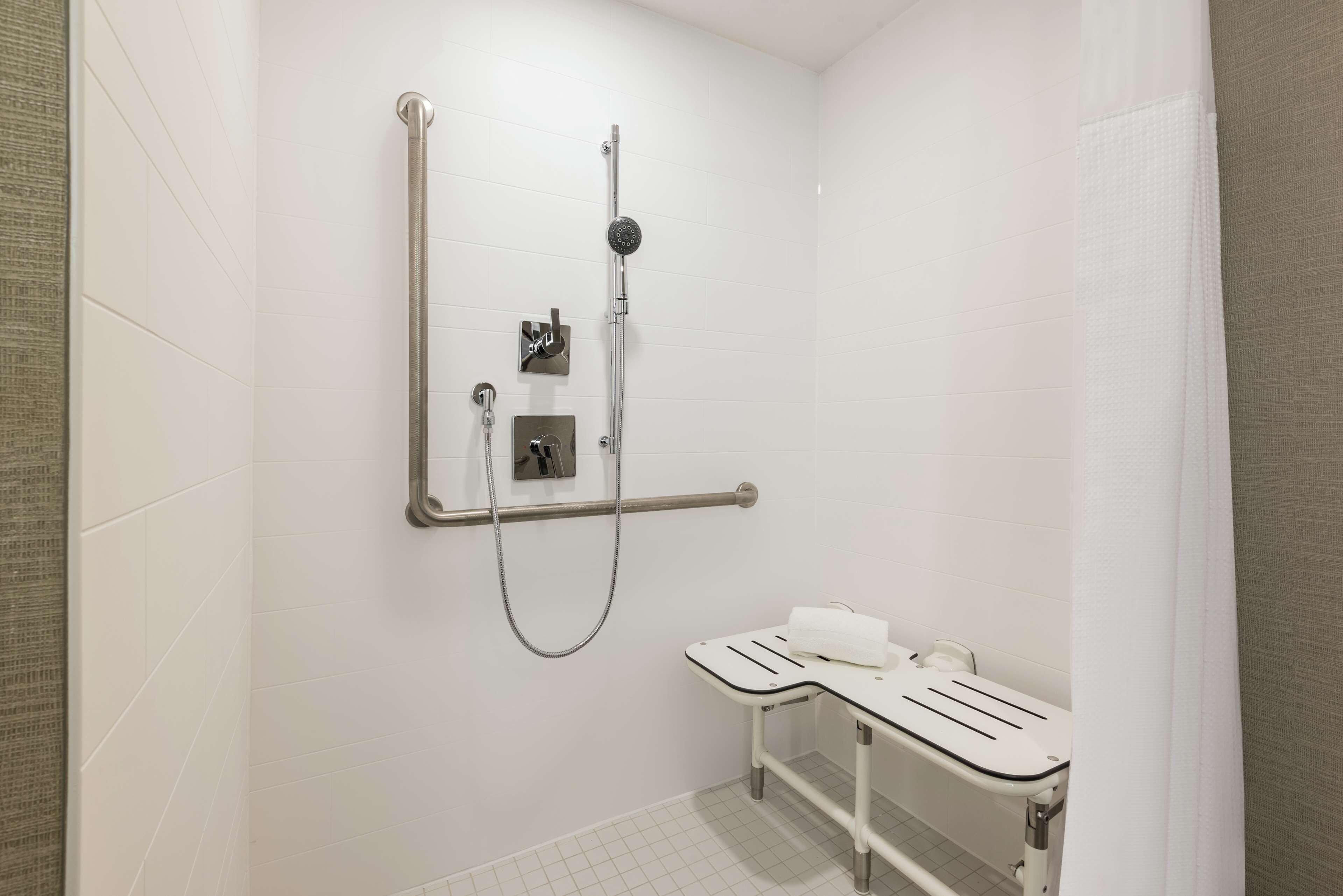 Une salle de bain avec une douche, une barre d’appui et un lavabo blanc.