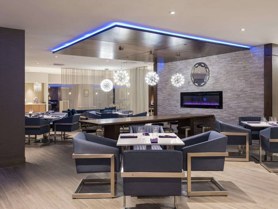 A modern dining area with a long table, cushioned seating, and a flat-screen TV mounted on the wall.