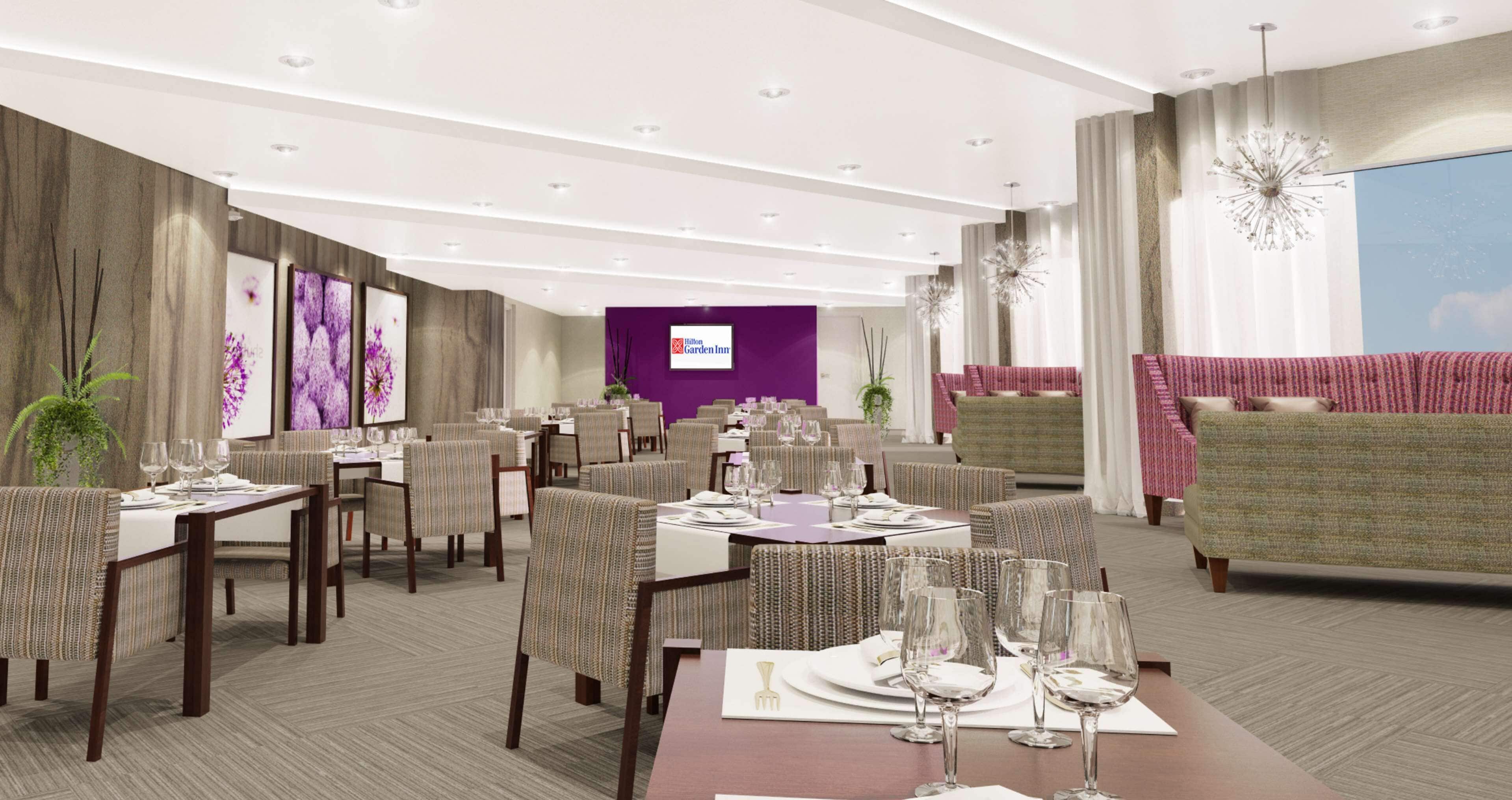 A hotel dining area with multiple tables set for dining, a reception desk, and a large window with a view.