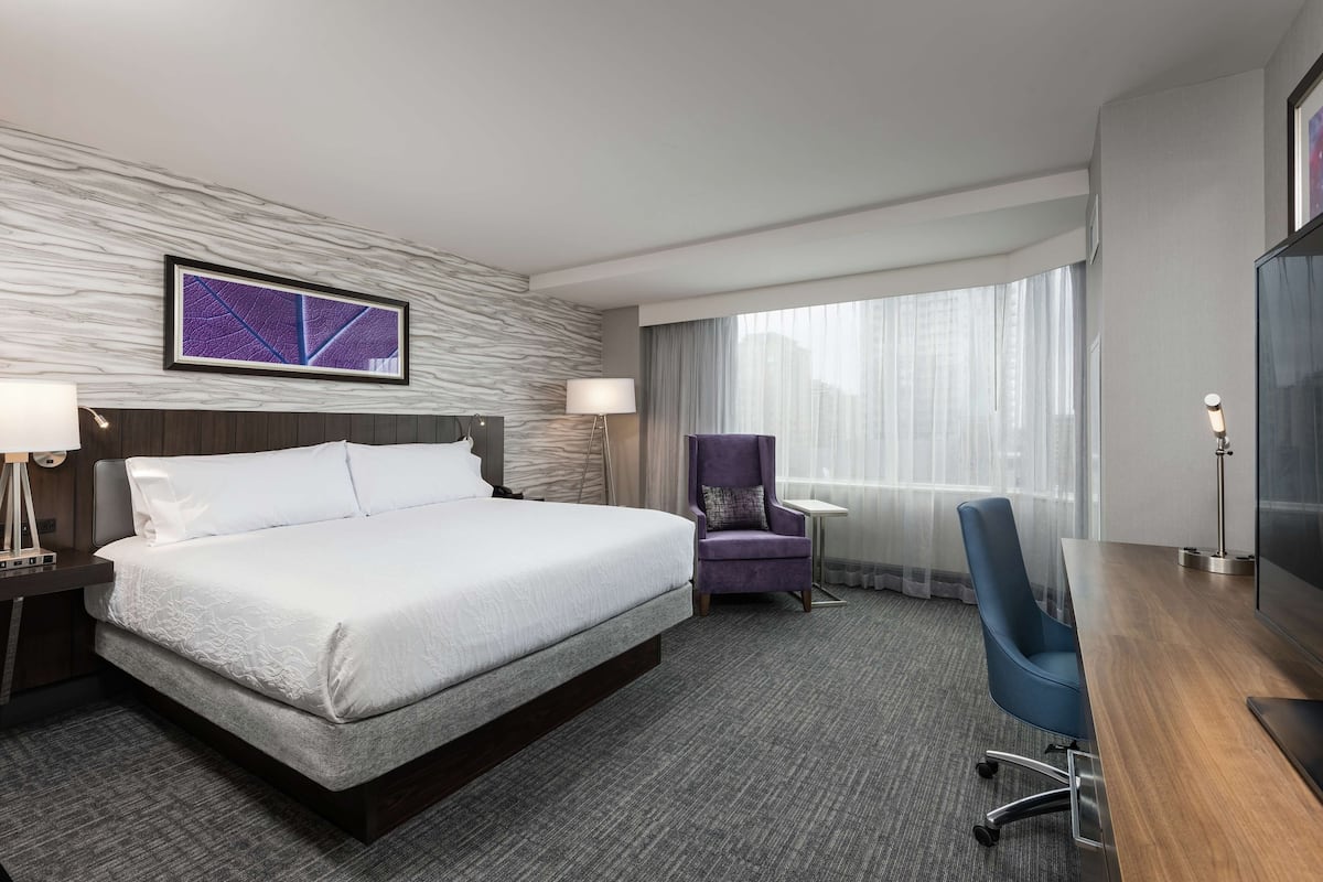 A hotel room with a large bed, a desk, a chair, and a window with curtains.