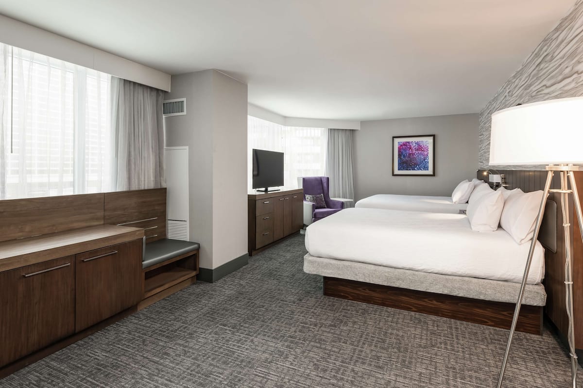 A hotel room with a bed, a desk, a chair, a TV, and a painting on the wall.