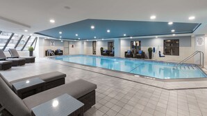 Une piscine intérieure dotée de chaises longues et d’un sol carrelé.