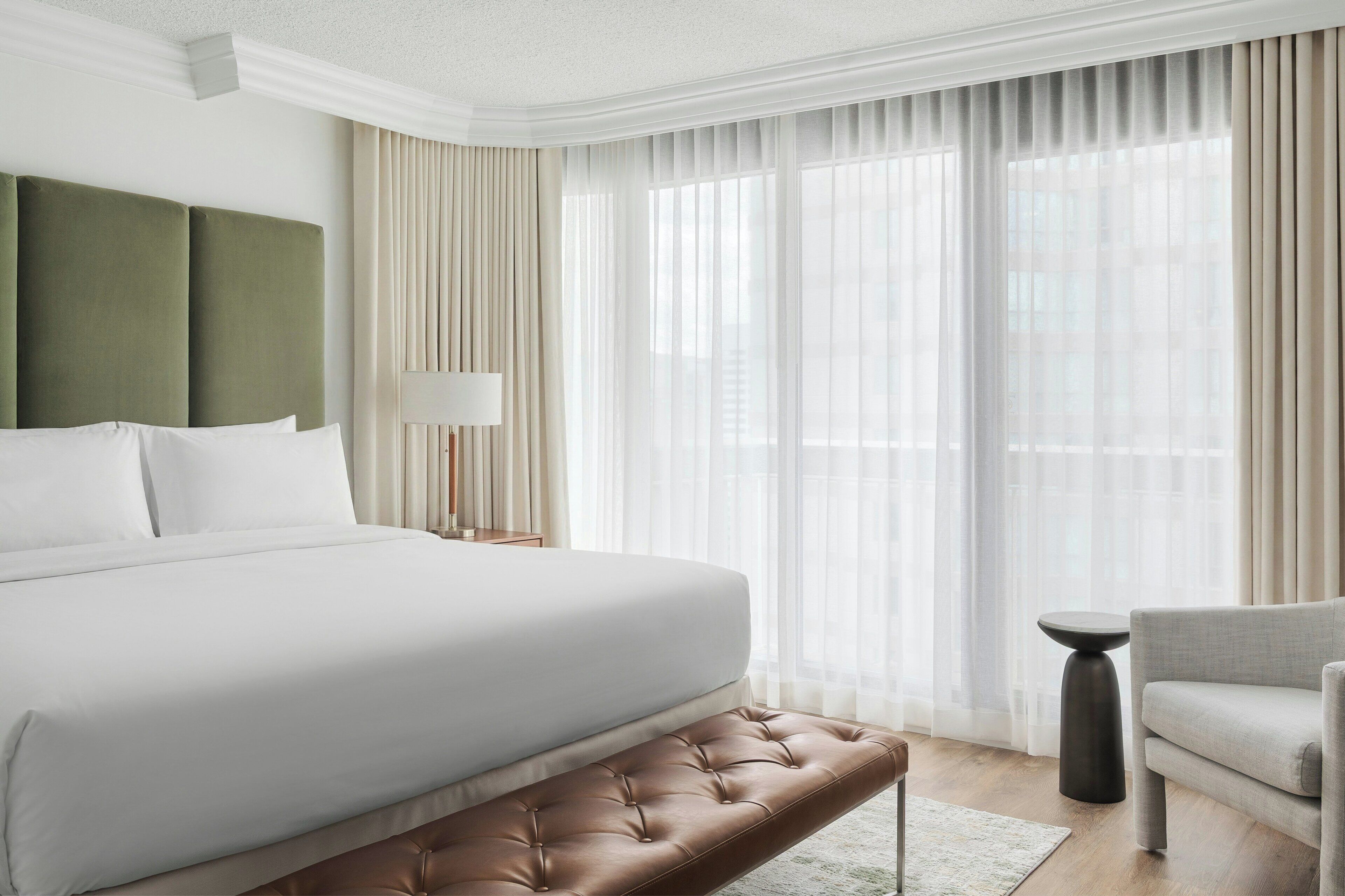 Een hotelkamer met een groot bed, een bankje, een stoel en een lamp.