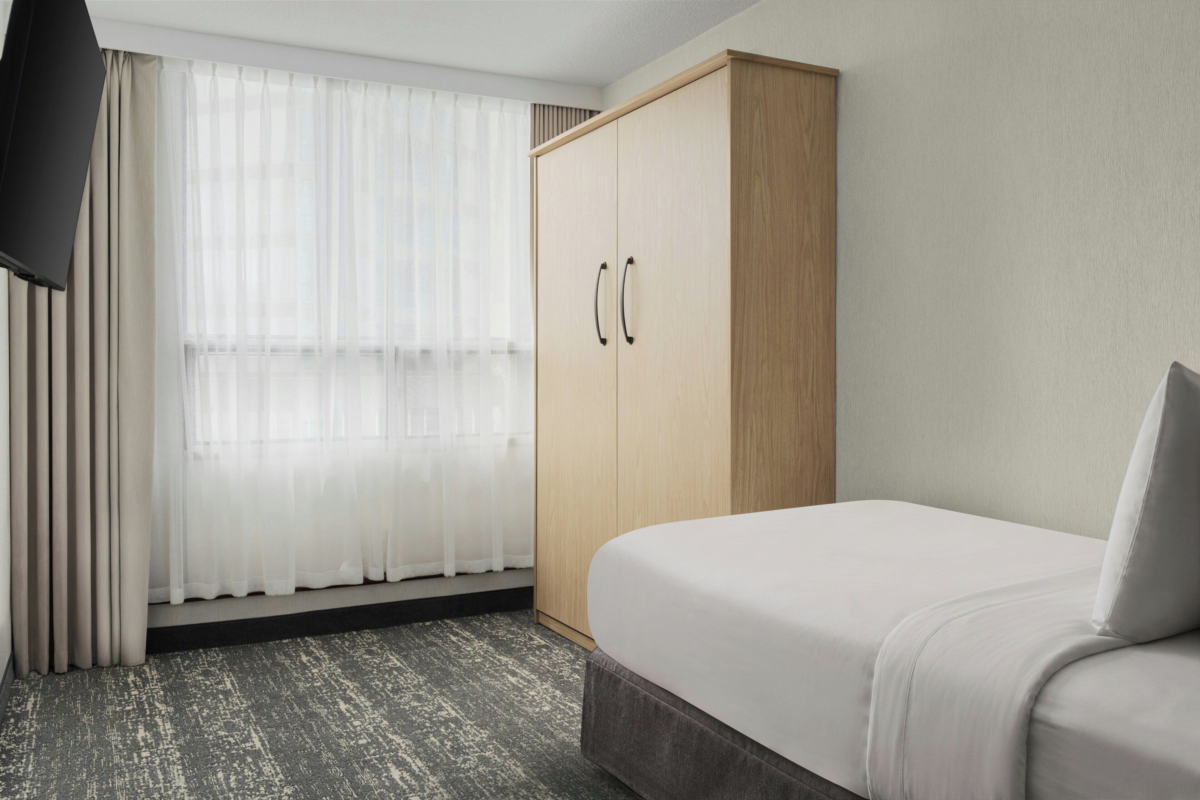 A hotel room with a bed, a wardrobe, and a window with sheer curtains.