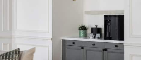 A modern kitchen with a white countertop, grey cabinets, a wall-mounted light fixture, and a small potted plant.