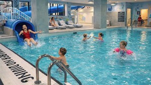 An indoor swimming pool with a slide, lounge chairs, and a lifeguard stand.