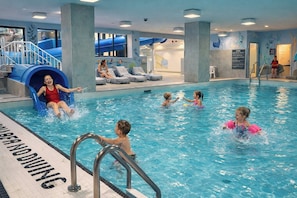An indoor swimming pool with a slide, lounge chairs, and a lifeguard stand.