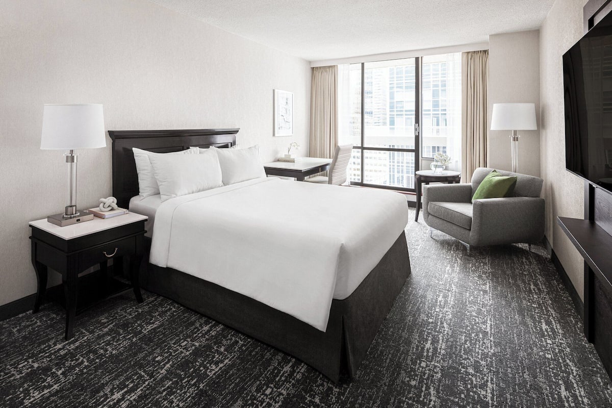 A hotel room with a large bed, a desk, a chair, and a TV.