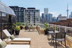 Terraza en la azotea con mobiliario exterior, plantas en macetas y vistas al horizonte de la ciudad.