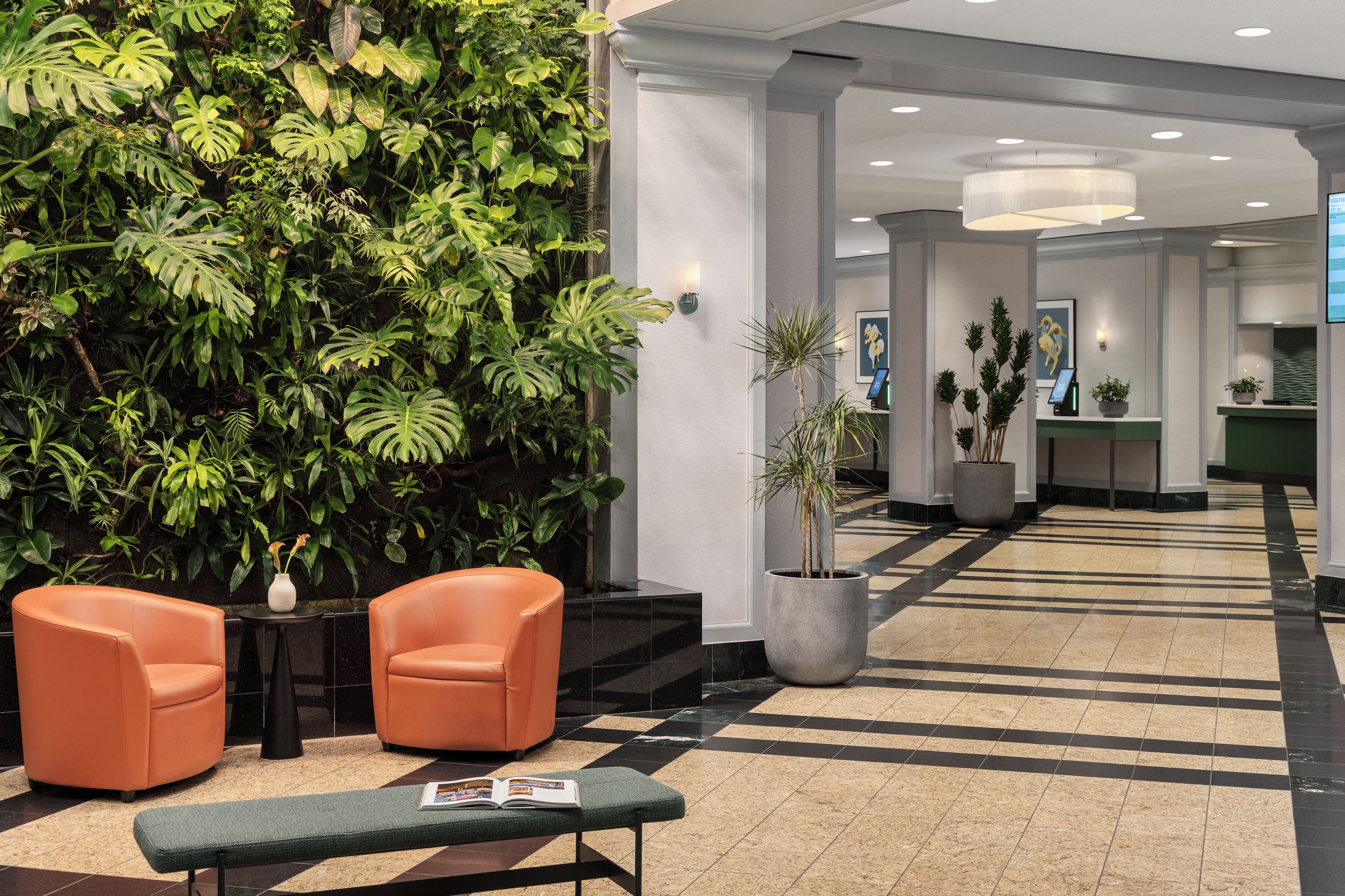 A reception area with a green wall of tropical plants, two orange chairs, a bench, and a reception desk.