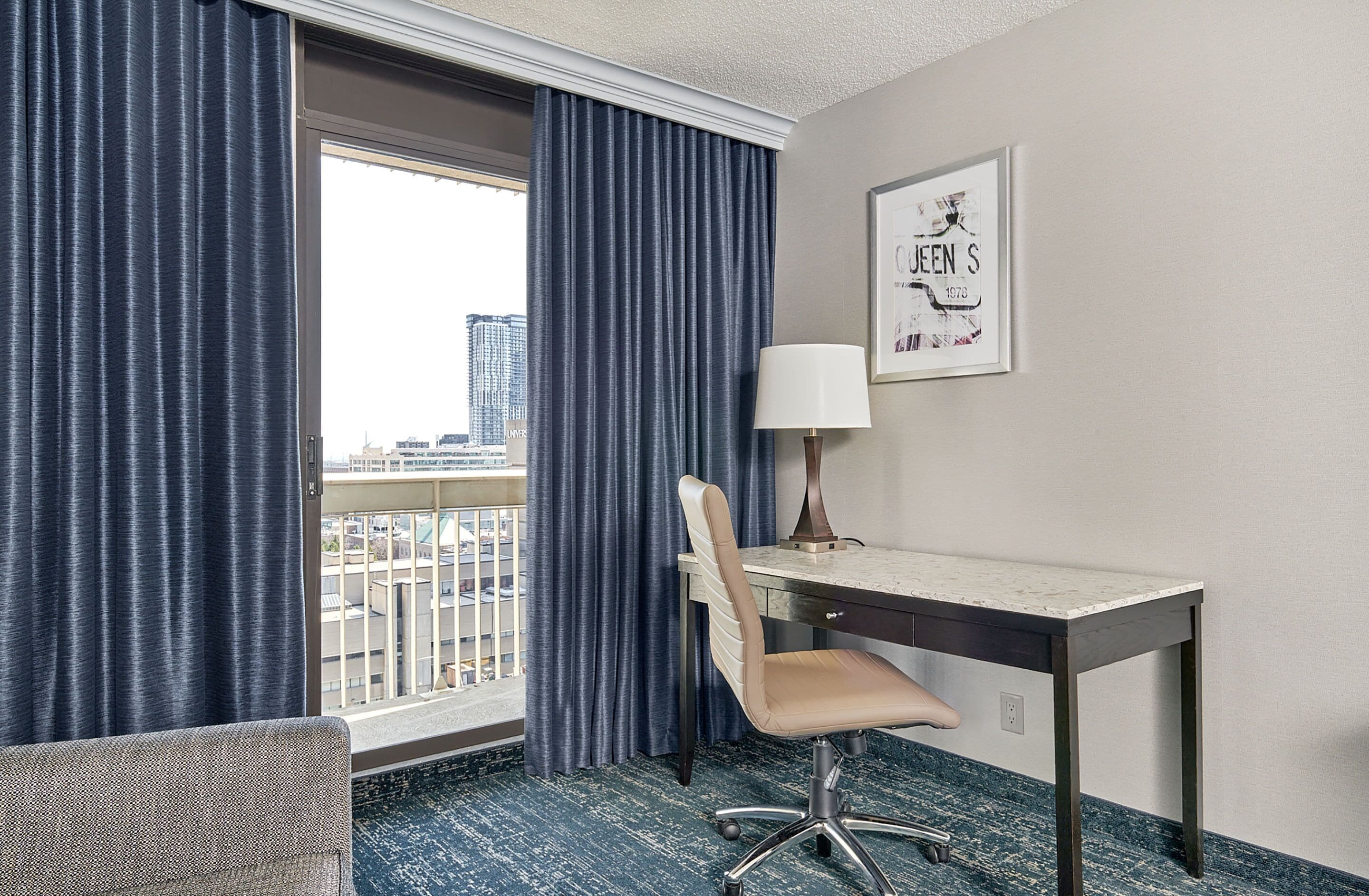 A hotel room with a desk, chair, and a window with curtains.
