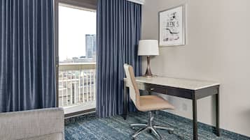 Una habitación de hotel con escritorio, silla y ventana con cortinas.