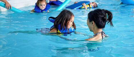 A swimming pool with children and adults in the water, some using floatation devices.