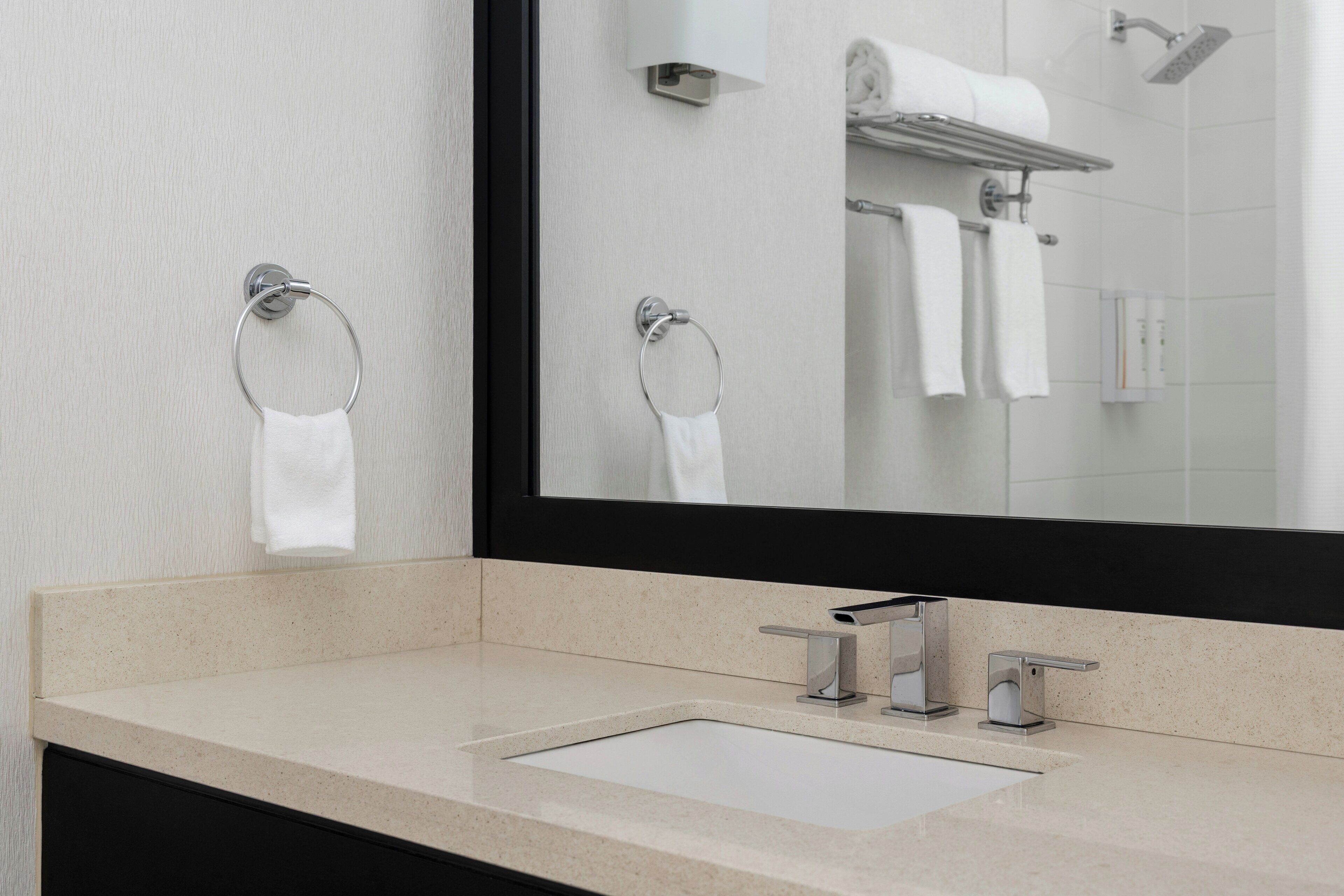 A bathroom with a large mirror, two towel rings, a sink, and a shower.