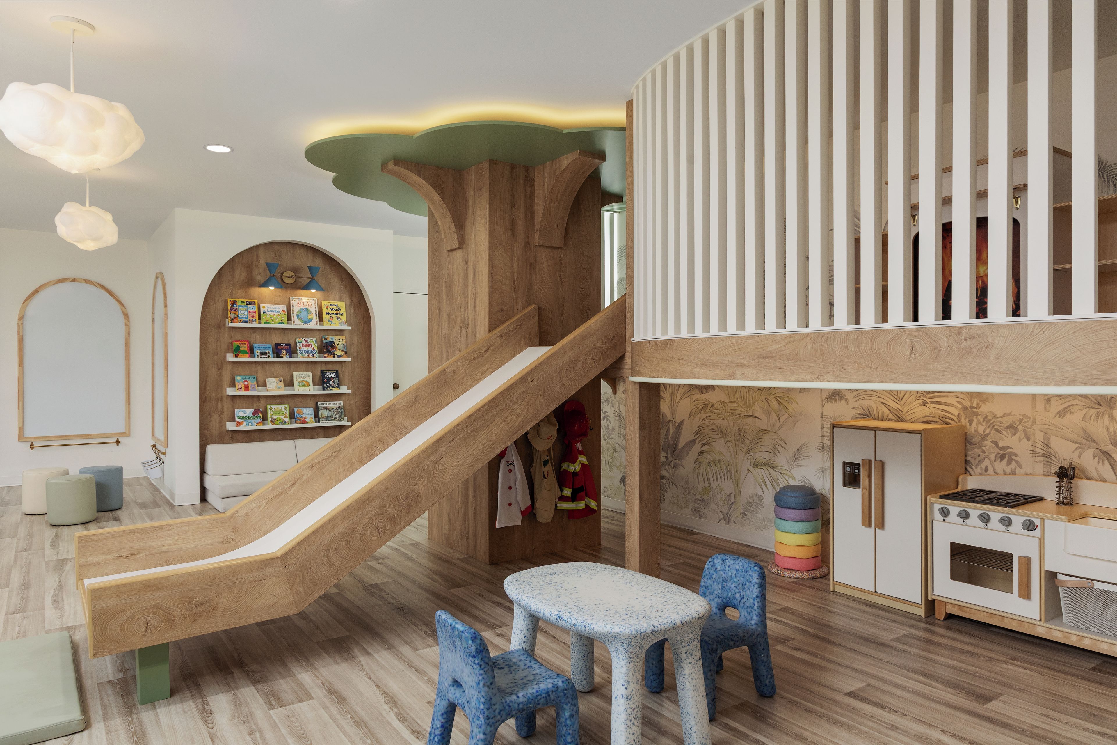 A children's play area with a slide, bookshelves, a small table, chairs, and a kitchen area with a stove.