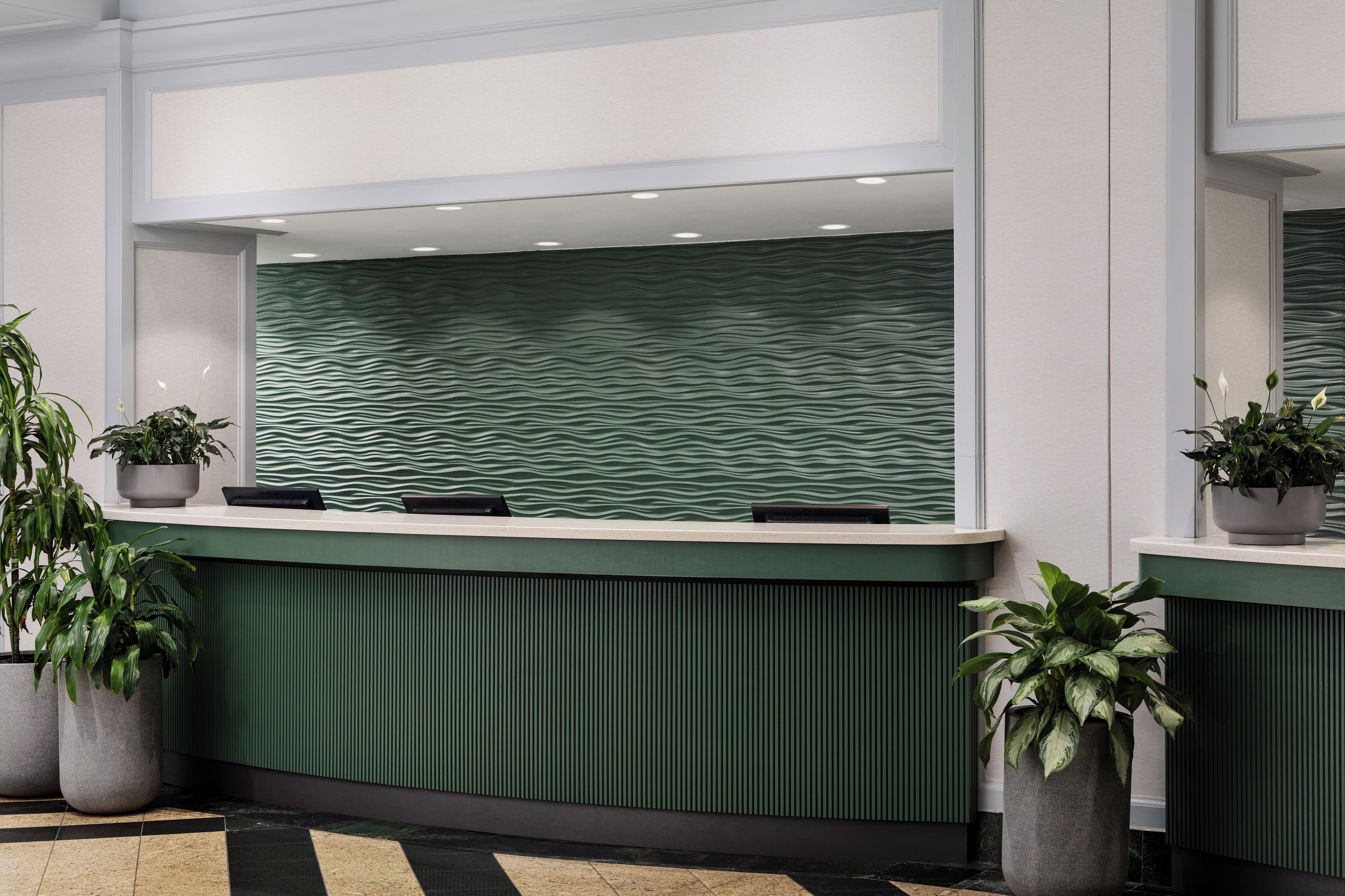 A reception desk with a green textured wall, potted plants, and a tiled floor.