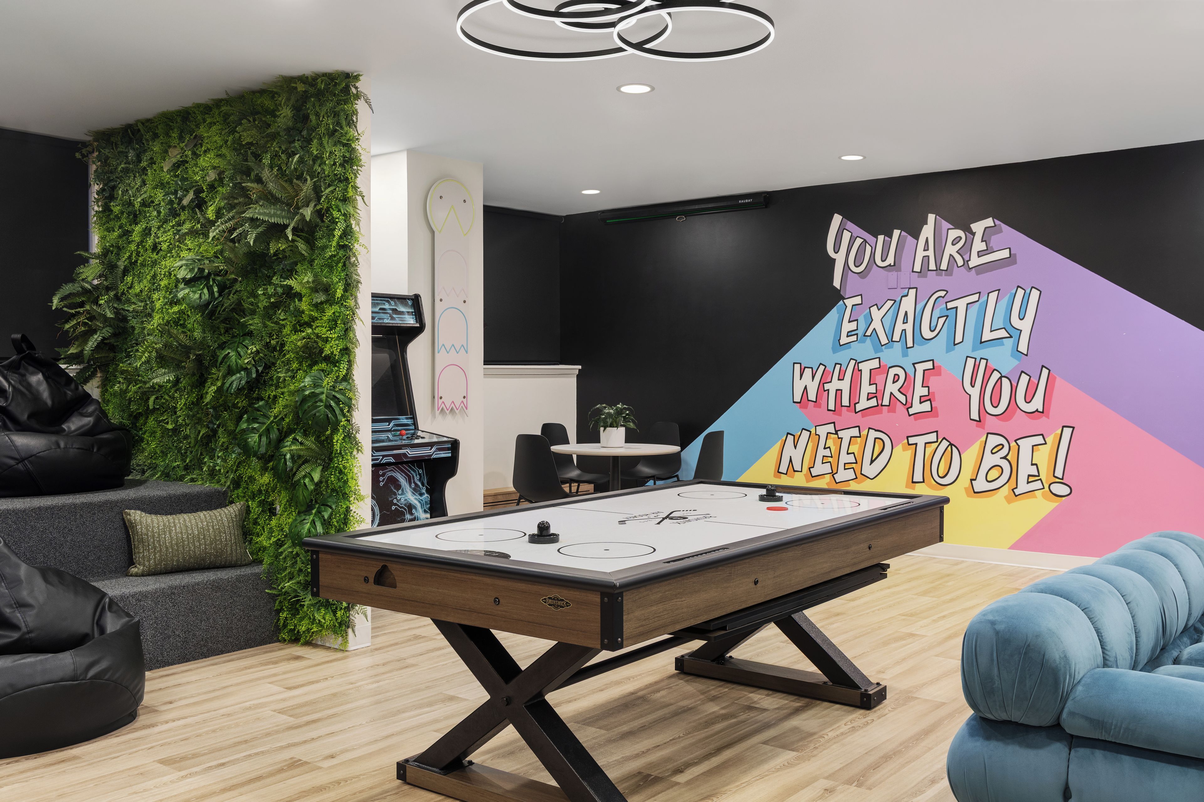 Ein Zimmer mit Billardtisch, einer grünen Wand mit Pflanzen, einer Wandbeschriftung und moderner Möbel.