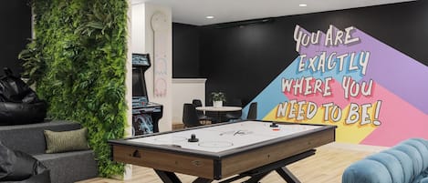 A room with a pool table, a green wall with plants, a message on the wall, and modern furniture.